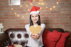 giovane donna sorridente che indossa un cappello rosso di babbo natale che mostra un modello a forma di cuore il giorno di natale, concetto di vacanza. foto