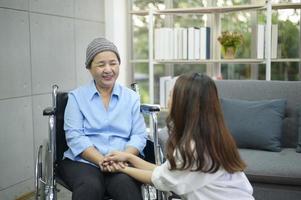donna malata di cancro che indossa una sciarpa per la testa seduta su sedia a rotelle che parla con sua figlia di supporto all'interno, concetto di salute e assicurazione. foto