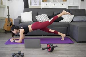 una donna sta facendo yoga e sta guardando tutorial di formazione online sul suo laptop in soggiorno, allenamento fitness a casa, concetto di tecnologia sanitaria. foto