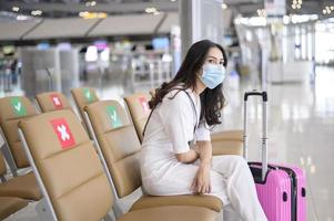 una donna viaggiatrice indossa una maschera protettiva nell'aeroporto internazionale, viaggia sotto la pandemia covid-19, viaggi di sicurezza, protocollo di allontanamento sociale, nuovo concetto di viaggio normale foto
