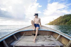 Vista dell'uomo in costume da bagno godendo sulla tradizionale barca tailandese a coda lunga sulla bellissima montagna e sull'oceano, isole phi phi, tailandia foto