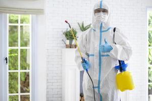 uno staff medico in tuta dpi sta usando spray disinfettante in soggiorno, protezione covid-19, concetto di disinfezione.