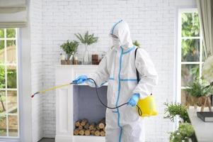 uno staff medico in tuta dpi sta usando spray disinfettante in soggiorno, protezione covid-19, concetto di disinfezione foto
