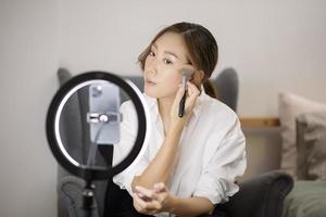 una bellissima blogger asiatica di trucco sta trasmettendo in diretta streaming come truccare il viso di bellezza nel suo concetto di casa, bellezza e tecnologia