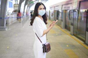 una giovane donna è in piedi sulla piattaforma della metropolitana, indossa una maschera facciale, protezione covid-19, nuovo concetto di viaggio normale.