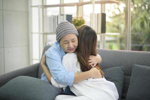 donna malata di cancro che indossa una sciarpa per la testa che abbraccia sua figlia di supporto all'interno, concetto di salute e assicurazione. foto