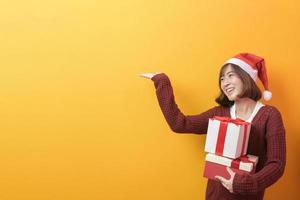 Ritratto di bella donna che indossa il cappello rosso di Babbo Natale che tiene una confezione regalo su sfondo per studio, concetto di Natale e Capodanno foto