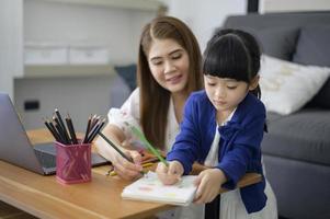 la mamma e la figlia felici asiatiche stanno usando il laptop per studiare online via Internet a casa. concetto di e-learning durante il periodo di quarantena. foto