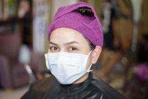 una giovane donna si taglia i capelli in un parrucchiere, indossa una maschera per la protezione covid-19, concetto di sicurezza del salone foto