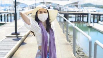una donna viaggiatrice indossa una maschera protettiva sul molo, viaggia sotto la pandemia covid-19, viaggi di sicurezza, protocollo di allontanamento sociale, nuovo concetto di viaggio normale