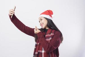 giovane donna sorridente che indossa un cappello rosso di Babbo Natale che si fa un selfie su sfondo bianco studio. foto