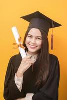 ritratto di bella donna felice in abito di laurea è in possesso di certificato di istruzione su sfondo giallo foto