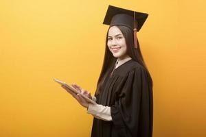 il ritratto di bella donna in abito di laurea tiene in mano un tablet su sfondo giallo foto