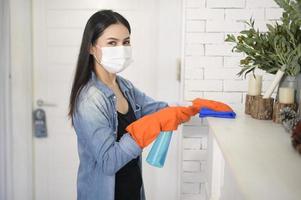 una donna con guanti per la pulizia che usa un disinfettante spray alcolico per pulire la casa, sano e medico, protezione covid-19 a casa concetto
