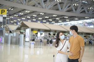 una coppia asiatica indossa una maschera protettiva nell'aeroporto internazionale, viaggia sotto la pandemia covid-19, viaggi di sicurezza, protocollo di allontanamento sociale, nuovo concetto di viaggio normale. foto