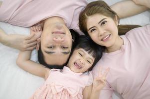 vista dall'alto di una famiglia asiatica felice che indossa un ritratto di camicia rosa sul letto bianco al coperto foto