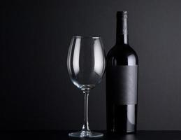 bottiglia di vino rosso con un bicchiere su sfondo nero foto