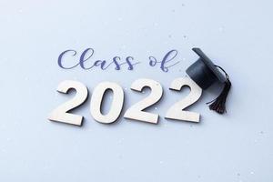 classe 2022 con berretto laureato su legno numero 2022 su sfondo grigio con glitter foto