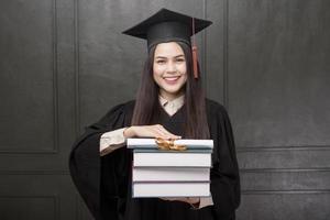 ritratto di giovane donna in abito di laurea sorridente e tifo su sfondo nero foto