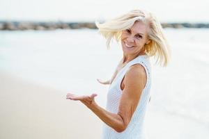felice donna matura che cammina sulla spiaggia, trascorrendo il suo tempo libero, godendosi il suo tempo libero foto