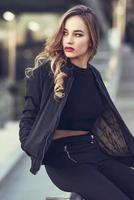 bella ragazza che indossa una giacca nera seduta in strada.