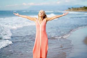 bella donna anziana che allarga le braccia su una bellissima spiaggia, trascorrendo il suo tempo libero. foto