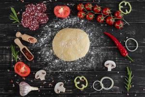 pasta cruda per pizza con ingredienti e spezie su sfondo nero foto