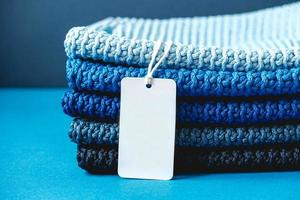 pila di materiale lavorato a maglia da fili di colori blu scuro, azzurro, grigio con cartellino del prezzo in bianco su sfondo blu foto