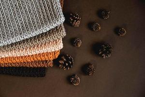 pila di materiale a maglia da fili di colori marrone, arancione, grigio con pigne su sfondo marrone foto