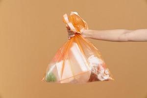 donna che tiene il sacchetto della spazzatura di plastica arancione