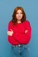 donna zenzero perplessa che indossa un maglione rosso in posa con le braccia incrociate foto