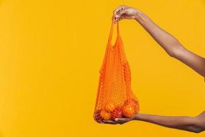 donna africana che tiene un sacchetto di frutta arancione riutilizzabile foto
