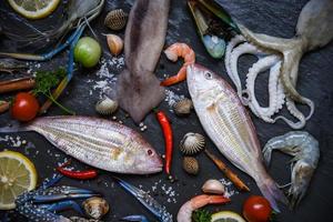 frutti di mare crudi freschi con erbe e spezie limone su sfondo scuro piatto di frutti di mare con crostacei gamberetti gamberi guscio di granchio foto