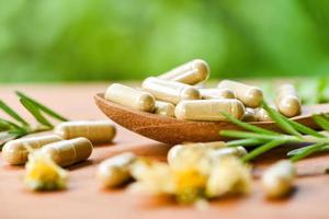 capsule di erbe da erbe stile di vita sano - erboristeria estratto dalla natura farmaco non tossico prodotto biologico su cucchiaio di legno e rosmarino di fiori selvatici su sfondo verde foto