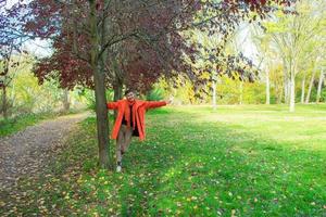 donna con mantello arancione e braccia aperte accanto a un albero foto