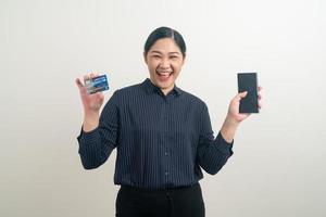 donna asiatica che utilizza smartphone con la mano che tiene la carta di credito foto