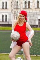 la bionda in forma rossa con una palla al cancello del campo di calcio. foto