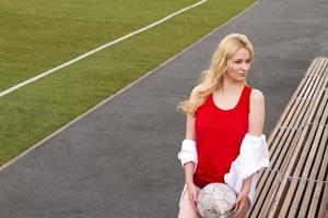 bionda con una palla sul campo di calcio in divisa rossa. foto