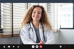 sorridente, allegra donna caucasica medico che guarda la telecamera mentre si incontra online con il paziente, concetti di servizio di videochiamata di consulenza medica domiciliare foto