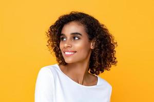 Ritratto ravvicinato di giovane bella donna afroamericana sorridente che pensa mentre guarda felicemente il lato in uno sfondo giallo studio isolato foto