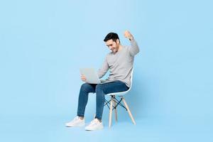 sorpreso giovane uomo caucasico guardando il computer portatile e alzando il pugno facendo sì gesto isolato su sfondo azzurro foto