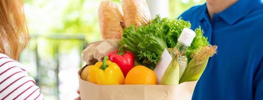 uomo di consegna del negozio di alimentari in uniforme blu che consegna cibo a una cliente donna a casa, dimensioni banner foto