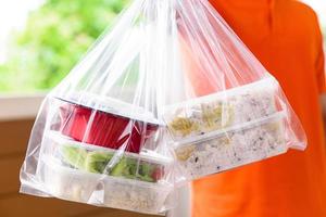 scatole di cibo asiatico in sacchetti di plastica consegnate al cliente a casa dal fattorino in uniforme arancione