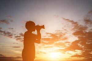 silhouette di un giovane uomo che tiene la macchina fotografica, allunga le braccia durante il tramonto. foto