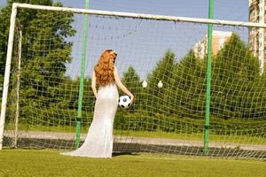 una ragazza con i capelli rossi sta alla porta di calcio con la schiena e la palla. foto