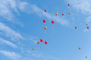 tanti palloncini rossi e dorati volano sotto il cielo azzurro e nuvole bianche foto