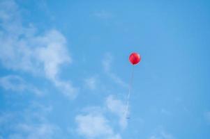 un palloncino rosso che vola sotto il cielo blu e nuvole bianche foto