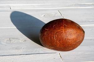 cocco intero maturo senza buccia dura con ombra su fondo di legno bianco, primo piano minimalismo vibrante foto