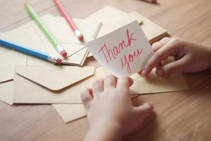 mano del bambino che tiene la lettera di ringraziamento sul tavolo foto