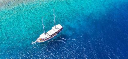 ancoraggio di yacht in acque turchesi cristalline di fronte all'isola tropicale, stile di vita ricreativo, snorkeling. vista aerea dello yacht all'ancora su acque turchesi, attività di lusso, tour delle Maldive foto